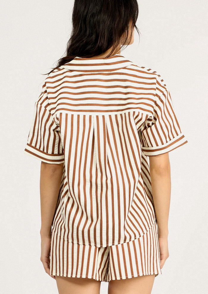 A person wearing a short sleeve button front shirt in cream and brown stripe.